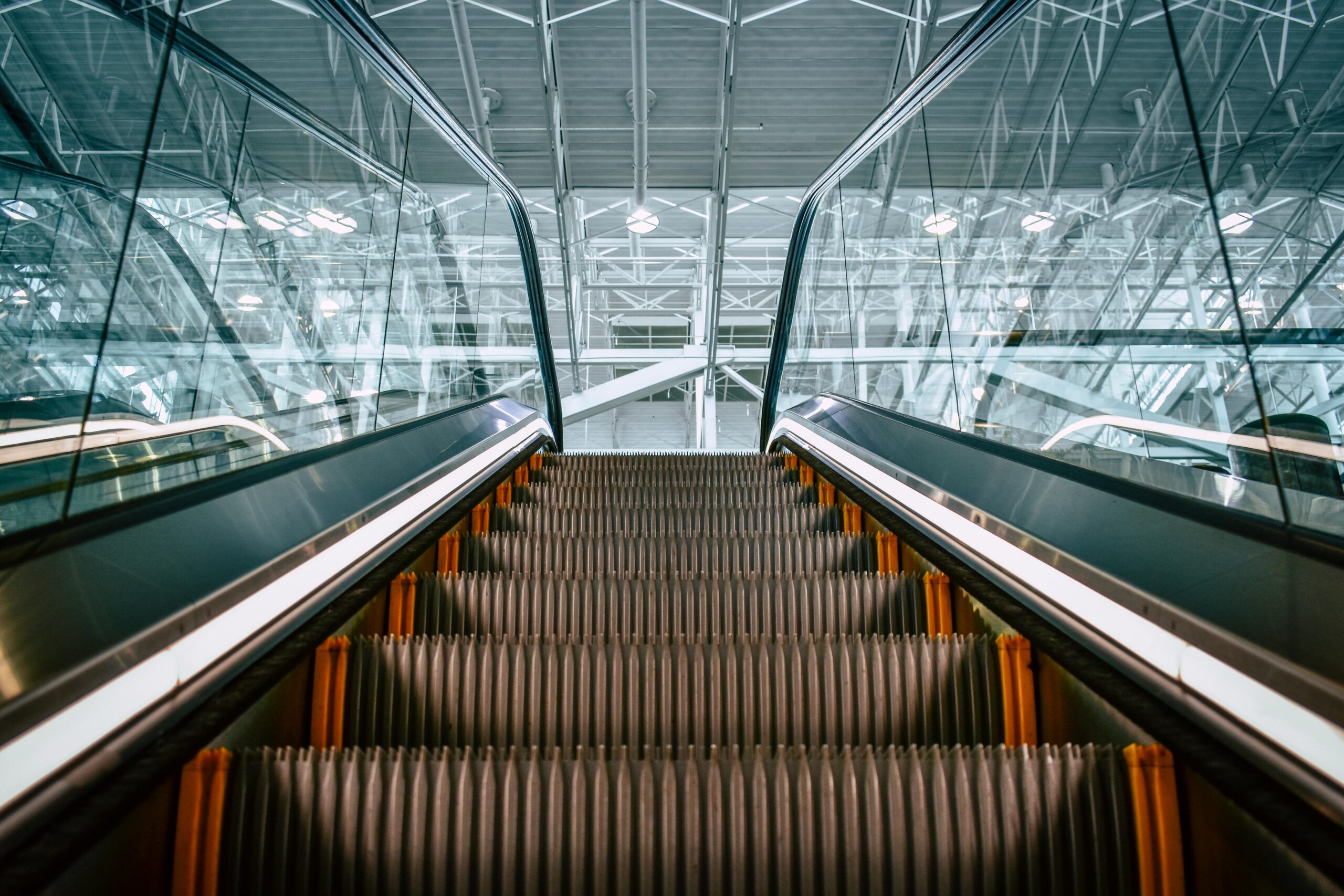 Low angle shot of a modern escalator inside a building, featuring steel framework and glass panels.